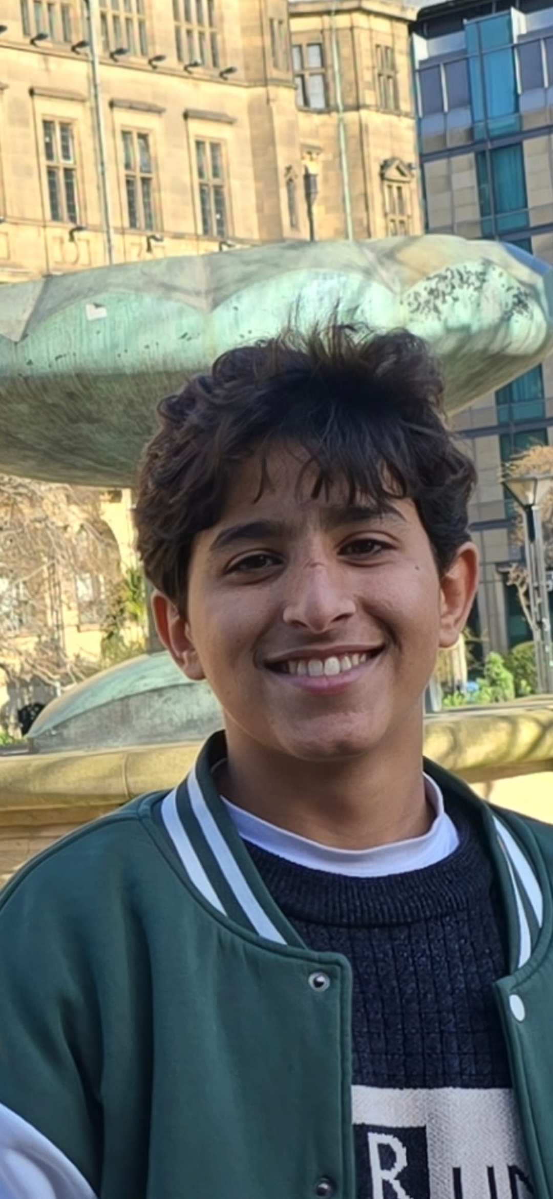 a 16-year-old boy wearing a green jacket smiles at the camera