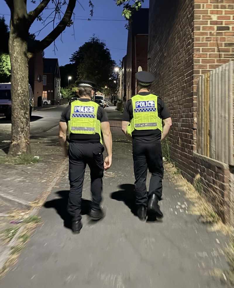 Two officers in high visibility uniforms carry out a patrol walking up a a street in Page Hall