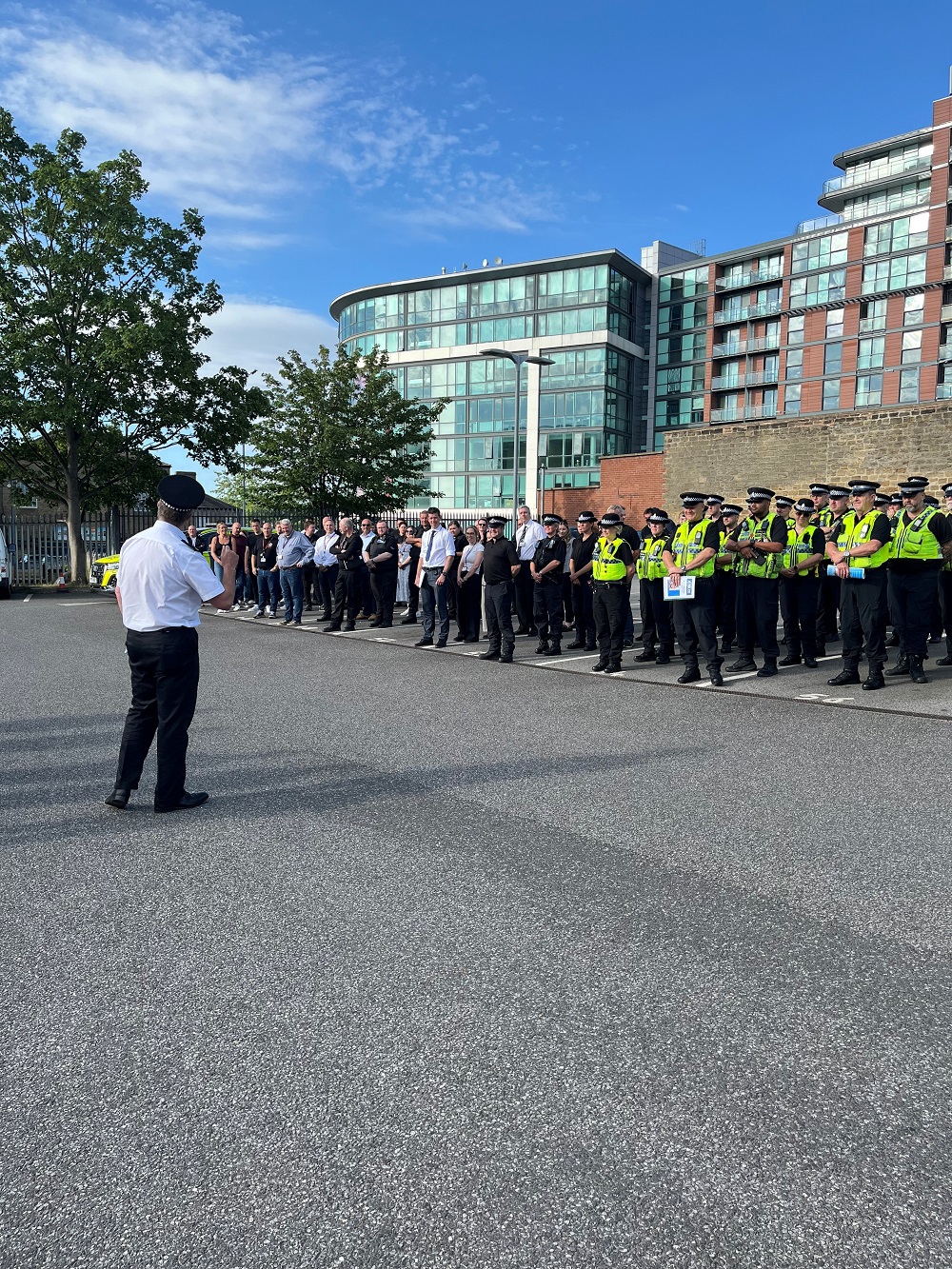 A group of police officers stand outside while being briefed by a superintenden