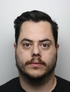 Aiden Evans is a white man with black hair and facial hair. He is standing in front of a white background