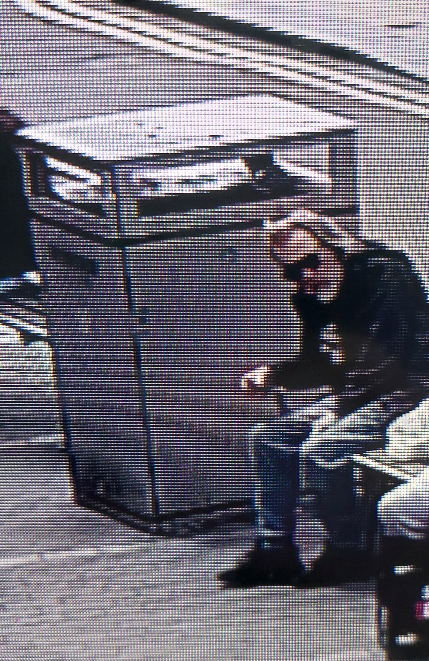 CCTV image of a white man wearing sun glasses and dark clothing sat on a bench