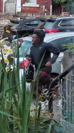 An image of a black man wearing a black Nike jumper, red trousers and carrying a black carrier bag running down a street