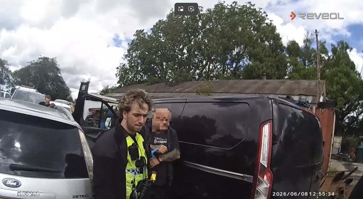 A screenshot from an officer's body-worn video camera showing a man being arrested by an officer at a car scrap yard