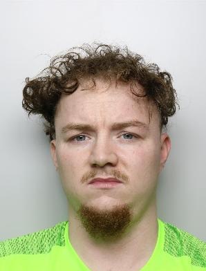 Nathan Peacock is a white man with curly hair and wearing a green sports top. He is standing in front of a white background for a custody picture