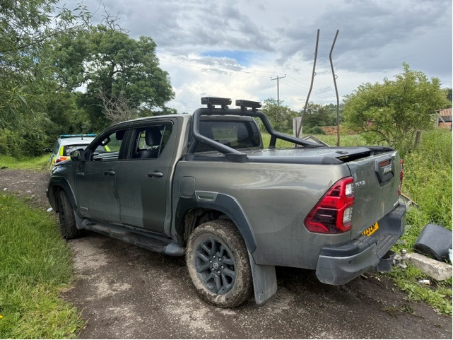 A black pick-up truck in the foreground, with a police car in front of it in the background parked on grass land
