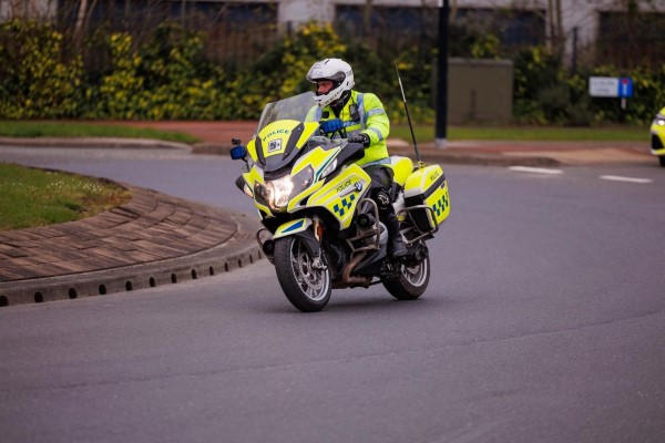 A UK police officer on a yellow and white BMW motorcycle, wearing a high-visibility jacket and white helmet.