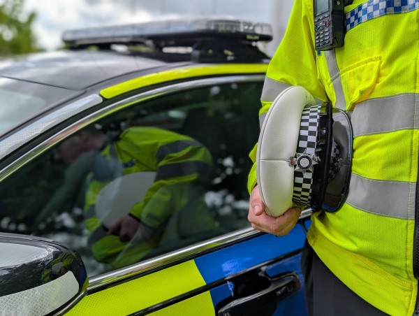 A police officers hands holding a traffic hat, white on top with a police car behind