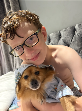 A young boy wearing glasses cuddling a small brown dog