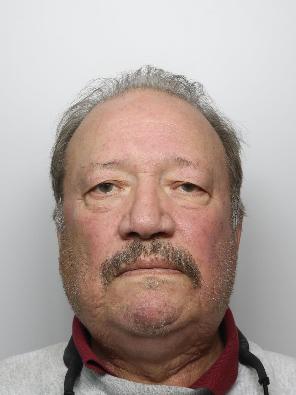 Paul Mundy is a white man in his 70s with a moustache and grey hair. He is standing in front of a white background for a custody picture