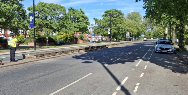 A photo of a police officer standing on the left hand side with a police car on the right hand side
