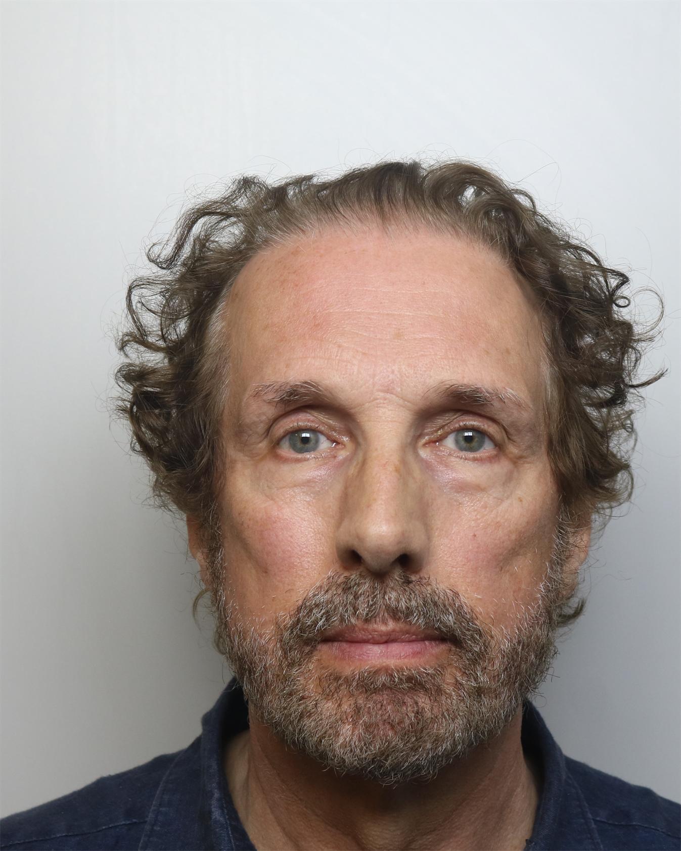 A head-and-shoulders portrait of a middle-aged man with curly brown hair, a grey-flecked beard, and a neutral expression.