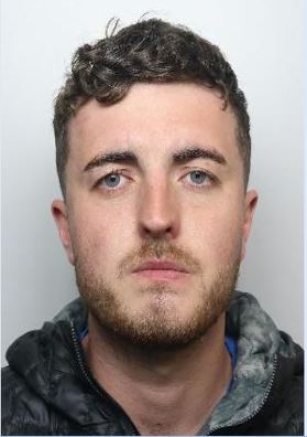 Mugshot of a white male with brown hair and brown beard wearing a black puffer coat